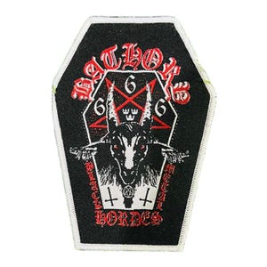 Op de afbeelding: Zwart doodskistvormig embleem met een witte rand. Het embleem toont een geitenkop met een pentagram, het nummer 6 en de woorden "SATLOK" en "BLACK METAL HORDES" in rode letters. Boven de geitenkop staat een kleine kroon.