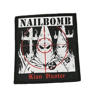 May include: Black square patch featuring the word "NAILBOMB" in white. Two hooded figures are within a red target. The text "Klan Hunter" is in red at the bottom. The patch has a black border.