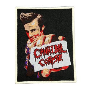 Può includere: Toppa ricamata con sfondo nero e bordo color crema. Presenta una persona che tiene in mano un cartello con le parole "CANNIBAL CORPSE" in lettere rosse gocciolanti. L'immagine è stilizzata.