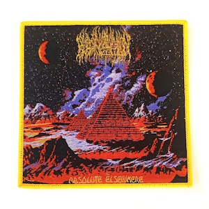 Puede incluir: Parche cuadrado con borde amarillo que presenta un paisaje surrealista con pirámides rojas, un cielo estrellado y el texto "ABSOLUTE ELSEWHERE". El diseño incluye un tema celestial con dos lunas crecientes.