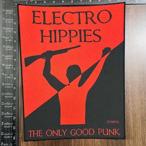 May include: A rectangular patch with a red and black split design. The top half is red with the words "ELECTRO HIPPIES" in black. A black silhouette of a person holding a rifle and raising a fist is in the center. The bottom half is black with the text "THE ONLY GOOD PUNK".