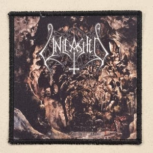 May include: Square patch with a black border featuring the word "Unleashed" in a gothic font above an inverted cross. The background depicts a dark, detailed scene with the text "Shadows In The Deep".