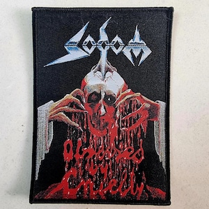 Könnte beinhalten: Schwarz-weiß gestickter Patch mit dem Bandnamen "SODOM" in silberner Schrift. Der Patch zeigt einen blutigen Schädel mit einem silbernen Blitz darüber.