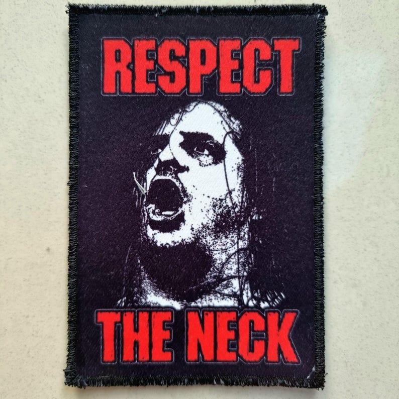以下が含まれることがあります： 赤いブロック体の文字で「RESPECT THE NECK」と書かれた黒い長方形のパッチ。パッチには、叫んでいる人の白黒画像が描かれています。パッチには黒いほつれた縁があります。