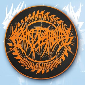 May include: A round black patch with orange text and design. The text reads "SLAM-MING BRUTAL-DEATHGRIND" in a stylized, jagged font. The design features a central, spiky graphic with a saw blade border.