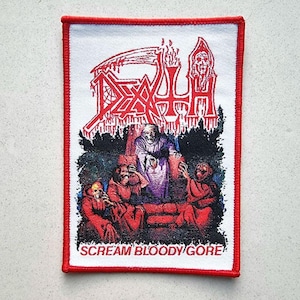 Op de afbeelding: Een rood, wit en zwart geborduurd patch met het woord "DEATH" in grote, vetgedrukte letters. De patch heeft een schedel en gekruiste beenderen ontwerp en de tekst "SCREAM BLOODY GORE".