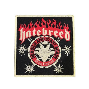 Pode incluir: Patch quadrado preto com a palavra "hatebreed" em chamas vermelhas. O patch apresenta um emblema circular com um design semelhante a um pássaro e as palavras "Rebuild and Start Again" e "Destroy Everything".