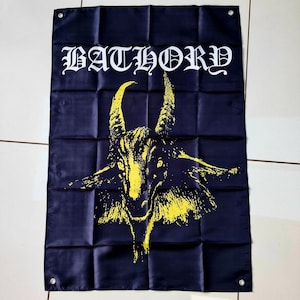 Könnte beinhalten: Dunkelblaue Flagge mit dem Wort "BATHORY" in weißen gotischen Buchstaben. Darunter eine gelbe Illustration eines Ziegenkopfes mit großen Hörnern. Die Flagge hat eine rechteckige Form.