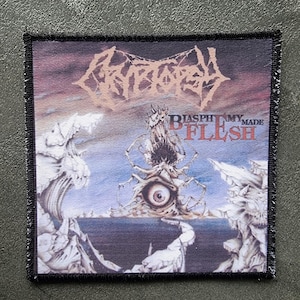May include: Square patch with a black border featuring the band name "Cryptopsy" in a stylized font. The artwork depicts a surreal landscape with an eye and the words "Blasphemy Made Flesh". The background has shades of blue, purple, and white.