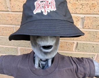 May include: Black bucket hat featuring the word "DEATH" in a red and white graphic. The hat is worn by a grey mannequin wearing a brown t-shirt.