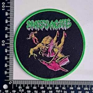 以下が含まれることがあります： 黒と緑の刺繍パッチで、白い文字で「Napalm Death」と書かれています。パッチの中央には、ピンクの手を持つ緑のモンスターがいます。