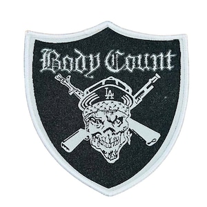 May include: Black and white patch with the words "Body Count" in gothic lettering. The patch features a skull wearing a hat with "LA" on it, crossed rifles, and a white border.