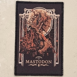 May include: A rectangular patch with a black border and a detailed illustration. The artwork features a figure with a staff, intricate details, and the word "MASTODON" at the bottom. The color palette includes shades of brown, orange, and cream.