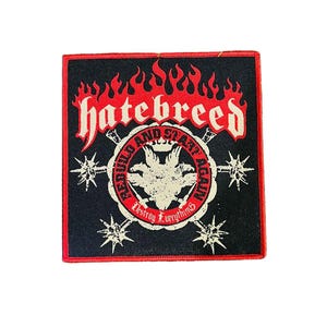 May include: Square black patch with red border featuring the word "hatebreed" in white, stylized flames, and a circular emblem with text and a three-headed creature. Additional starburst designs are on the sides.