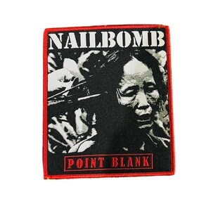 Puede incluir: Parche bordado en negro y rojo con la palabra "NAILBOMB" en blanco sobre una imagen en blanco y negro de una persona. El texto "POINT BLANK" está en rojo debajo. Borde rojo.