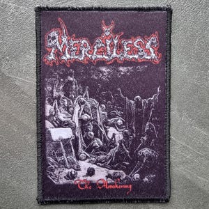 以下が含まれることがあります： 上部に赤と白のゴシック体で「Merciless」の文字が入った長方形のパッチ。パッチは、人物の暗いイラストと下部に「The Awakening」のテキストを特徴としています。