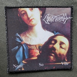 May include: Square patch featuring a printed image of a classical painting with a woman and a severed head. The patch has the band name "Cryptopsy" in white, stylized text, and the words "None So Vile". The patch has a black border.