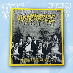 May include: A rectangular embroidered patch with a yellow border. The design features a black and white forest scene with figures holding chainsaws. The text AGATHOCLES appears in yellow at the top, and MINCING THROUGH THE MAPLES in yellow at the bottom.