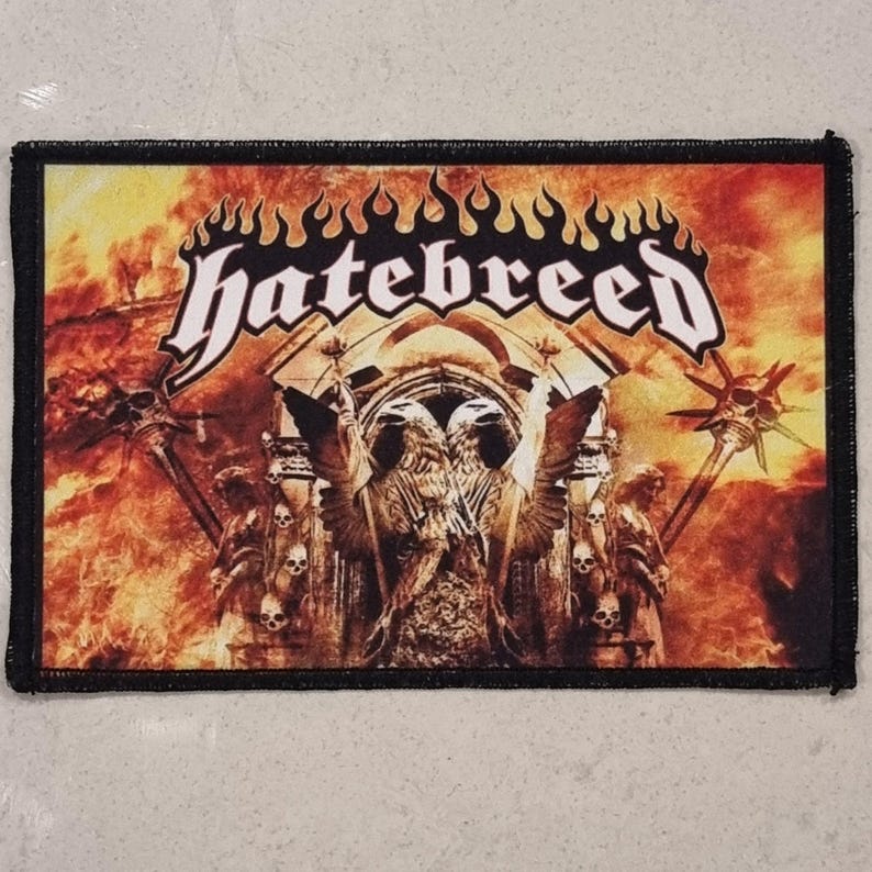 May include: A rectangular patch featuring the band name "hatebreed" in white, stylized text. The background depicts a fiery, orange and yellow scene with gothic architecture, statues, and skulls. The patch has a black border.