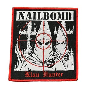 Op de afbeelding: Een zwart en rood geborduurd embleem met het woord "NAILBOMB" in witte blokletters bovenaan. Het embleem toont twee figuren in witte kappen met een rood vizier erover. De woorden "Klan Hunter" staan in rode letters onderaan.