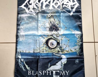 May include: Black banner with the word "CRYPTOSY" in white, stylized lettering. The banner features a grotesque illustration of a creature with a large eye and open mouth. The text "BLASPHEMY MADE FLESH" is at the bottom.