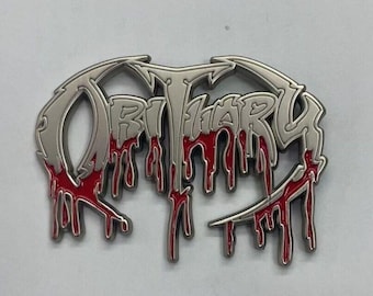 May include: A silver metal pin with the word "Obituary" in a dripping blood-like red font.