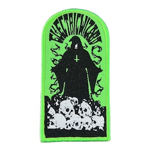 Puede incluir: Un parche rectangular con borde y fondo verdes. El parche presenta una silueta negra de una figura vestida con una túnica con una cruz, de pie sobre una pila de calaveras blancas. El texto "ELECTRIC WIZARD" está arqueado en la parte superior.