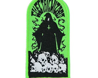 May include: A rectangular patch with a green border and background. The patch features a black silhouette of a robed figure with a cross, standing above a pile of white skulls. The text "ELECTRIC WIZARD" is arched across the top.