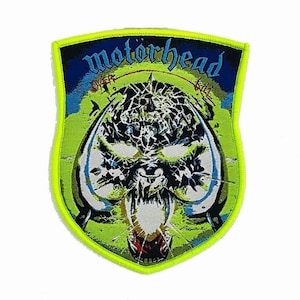 Op de afbeelding: Een schildvormige geborduurde patch met een neongele rand en een centrale afbeelding van een gestileerd schedelwezen. De tekst "motörhead" staat in het blauw bovenaan, met "over" en "kill" in het rood aan weerszijden van het schedelontwerp.