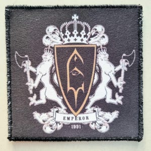 Puede incluir: Parche cuadrado negro con un emblema detallado. El emblema presenta un escudo con una corona, leones sosteniendo hachas y la palabra "EMPEROR" debajo. También está presente el año "1991". El parche tiene un borde negro.