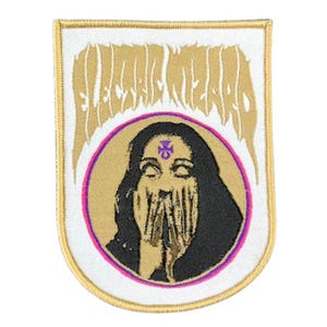 May include: Embroidered patch with a white background and gold trim. The patch features the text "ELECTRIC WIZARD" in gold, above a circular image of a person with black hair and a purple symbol on their forehead. The person's hands cover their face, and the circle is outlined in pink.