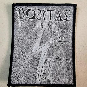 以下が含まれることがあります： ゴシック体で「PORTAL」と書かれた黒と白の刺繍パッチ。パッチには、スタイリッシュな稲妻のデザインが施されています。