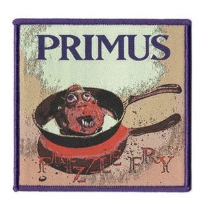 May include: A square embroidered patch with a purple border featuring the text PRIMUS at the top and FRIZZLE FRY at the bottom. The central graphic depicts a red frying pan containing a stylized, wide-eyed creature with sharp teeth.