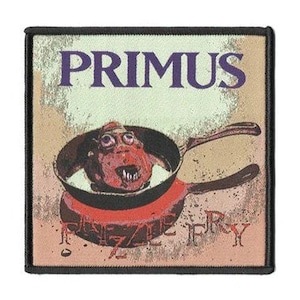 May include: A square embroidered patch with a black border featuring the text PRIMUS in purple at the top. Below, a red, bug-eyed creature with sharp teeth sits inside a black frying pan. The text FIZZLE FRY is printed in red at the bottom.