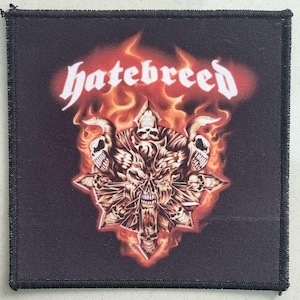 May include: Black square patch with the word "hatebreed" in white, stylized lettering. The patch features a flaming skull design with a star-like shape and multiple skulls. The edges are black and stitched.