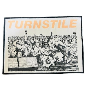 Puede incluir: Un parche rectangular con la palabra "TURNSTILE" en letras naranjas en la parte superior. El parche presenta una ilustración en blanco y negro de una multitud de personas, algunas cayendo y otras con los brazos levantados.
