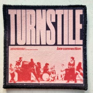 Könnte beinhalten: Ein quadratischer Aufnäher mit dem Wort "TURNSTILE" in großen, hellrosa Blockbuchstaben oben. Darunter ein rot-rosa Bild einer Band, die auftritt, mit den Worten "love connection" in kleinerer Schrift. Der Aufnäher hat einen schwarzen Rand.