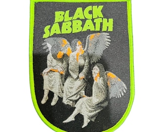 May include: Black Sabbath patch in a shield shape. The patch features the band's name in neon green block letters above a graphic of three winged figures. The patch has a black background and a neon green border.