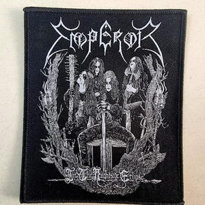Puede incluir: Parche negro con el nombre de la banda "Emperor" en letras góticas blancas. El parche muestra una ilustración en blanco y negro de los miembros de la banda rodeados por un bosque detallado y estilizado. El texto "In The Nightside Eclipse" está debajo.
