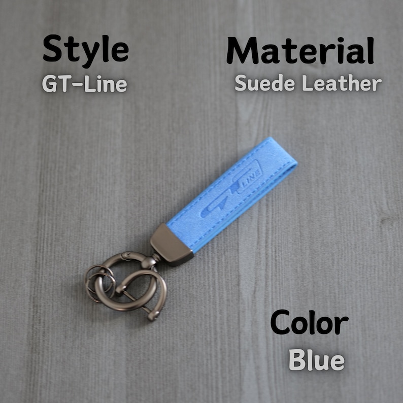 May include: A light blue suede leather keyring with a silver key ring and the text "GT-Line" embossed on the leather. The keyring is on a grey wooden surface.