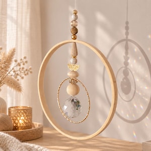 Könnte beinhalten: Ein hängendes Ornament mit einem großen Holzring, der einen kleineren, goldfarbenen, strukturierten Ring, ein facettiertes, klares Kristallprisma und eine vertikale Anordnung aus verschiedenen Holz-, Stein- und Metallperlen umschließt.