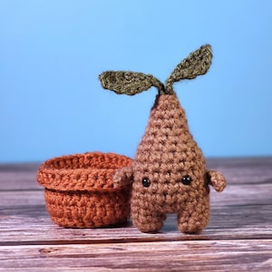 May include: A brown crocheted plant with a green crocheted leaf and a brown crocheted pot.