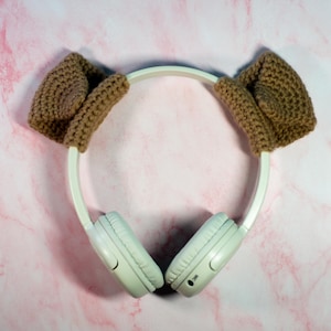 May include: White wireless headphones with brown knitted earmuffs. The headphones have a white headband and white earcups.