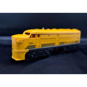 May include: A yellow model train locomotive featuring the number 221 printed in black on the side. The engine has a streamlined design with black undercarriage details, horizontal vents, and a cab window, presented in a side profile view.