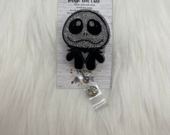 May include: A silver glitter badge reel featuring a black and white Jack Skellington character. The reel has a clear plastic badge holder and a silver clip. The card attached to the reel reads "Badge Reel Care" and includes instructions for cleaning and care.
