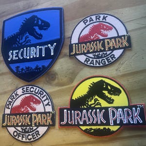 以下が含まれることがあります： ジュラシック・パークのロゴが刺繍されたパッチが4つ。パッチは色が異なり、"Security"、"Ranger"、"Officer"など、さまざまなテキストが書かれています。