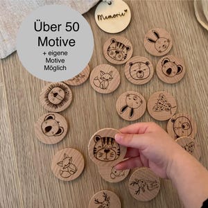 Könnte beinhalten: Holz-Memory-Spielsteine mit gravierten Tierillustrationen, darunter ein Tiger, ein Bär und ein Hase. Der Text "Über 50 Motive" ist sichtbar. Eine Hand hält eines der Teile. Die Spielsteine haben einen Durchmesser von ca. 5 cm.