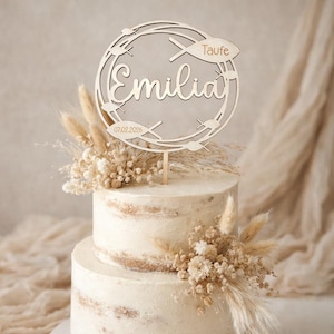 Op de afbeelding: Een taart met twee lagen en een houten taarttopper. De topper toont de naam "Emilia" in cursief, het woord "Taufe" en de datum 07.02.2026. De taart is versierd met gedroogde bloemen en tarwearen.