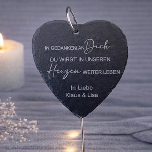Könnte beinhalten: Eine weiße Keramiktasse mit schwarzem Henkel und dem Text "But First, Coffee" in fetter, schwarzer Schrift. Die Tasse steht vor einem verschwommenen Hintergrund, der eine gemütliche Umgebung suggeriert.