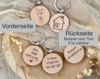 Könnte beinhalten: Vier Holzschlüsselanhänger mit verschiedenen Designs und Texten. Die Schlüsselanhänger liegen auf einer hellbraunen Oberfläche. Der Text auf den Schlüsselanhängern lautet "Familie Huber", "Stefan Anna Frieda", "Hans Anna Noah & Emil" und "Zu Hause ist kein Ort, das sind WIR".